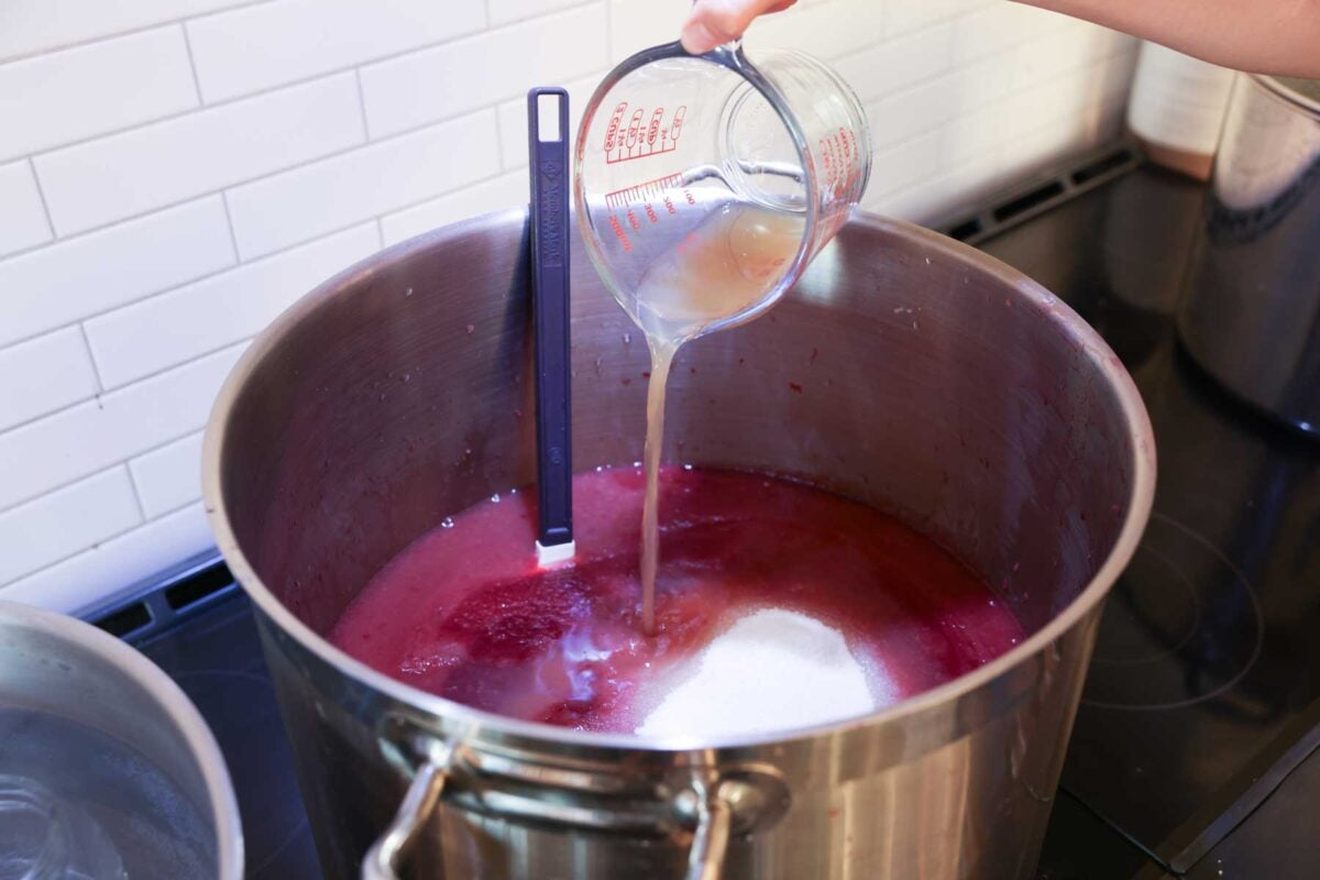 Adding canned lemon juice to a pot with cranberry applesauce and sugar.