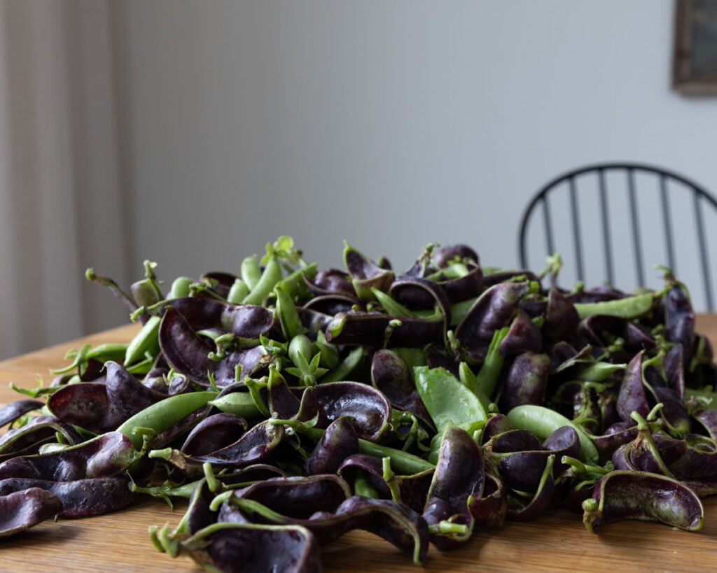 A pile of snow peas and snap peas on a table.