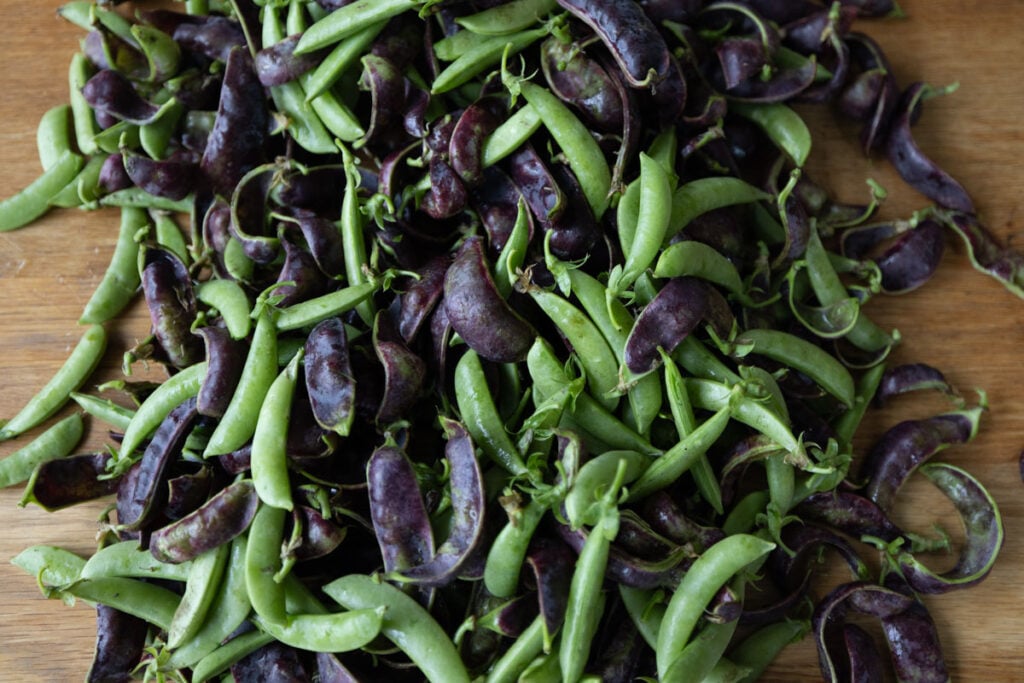 An arrangement of purple snow peas and green snap peas on a wood table.