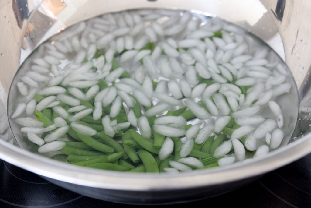A bowl filled with ice water and snap peas.