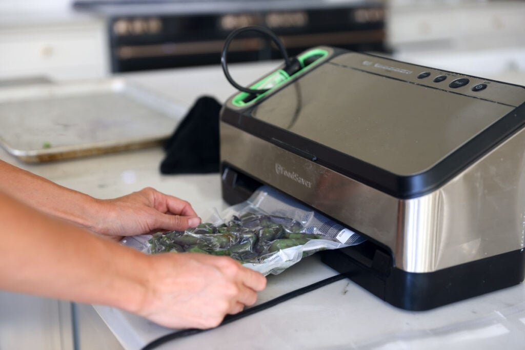 A plastic vacuum seal bag filled with frozen snow peas being vacuum sealed.
