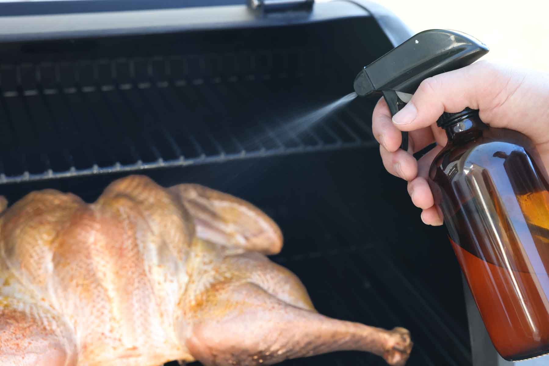 spraying a smoked turkey with apple cider vinegar during the cook