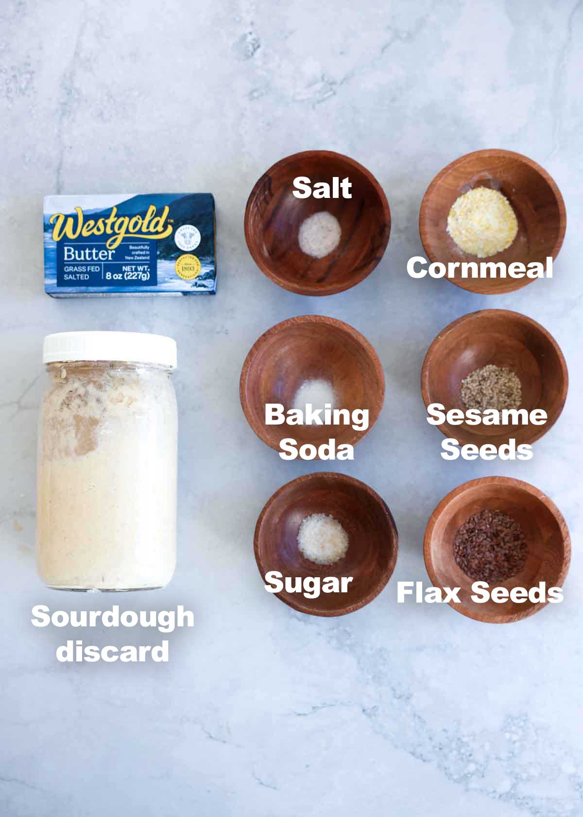 Ingredients for discard crackers like butter, sourdough discard, baking soda, salt, sugar, sesame seeds, flax seeds, and cornmeal.