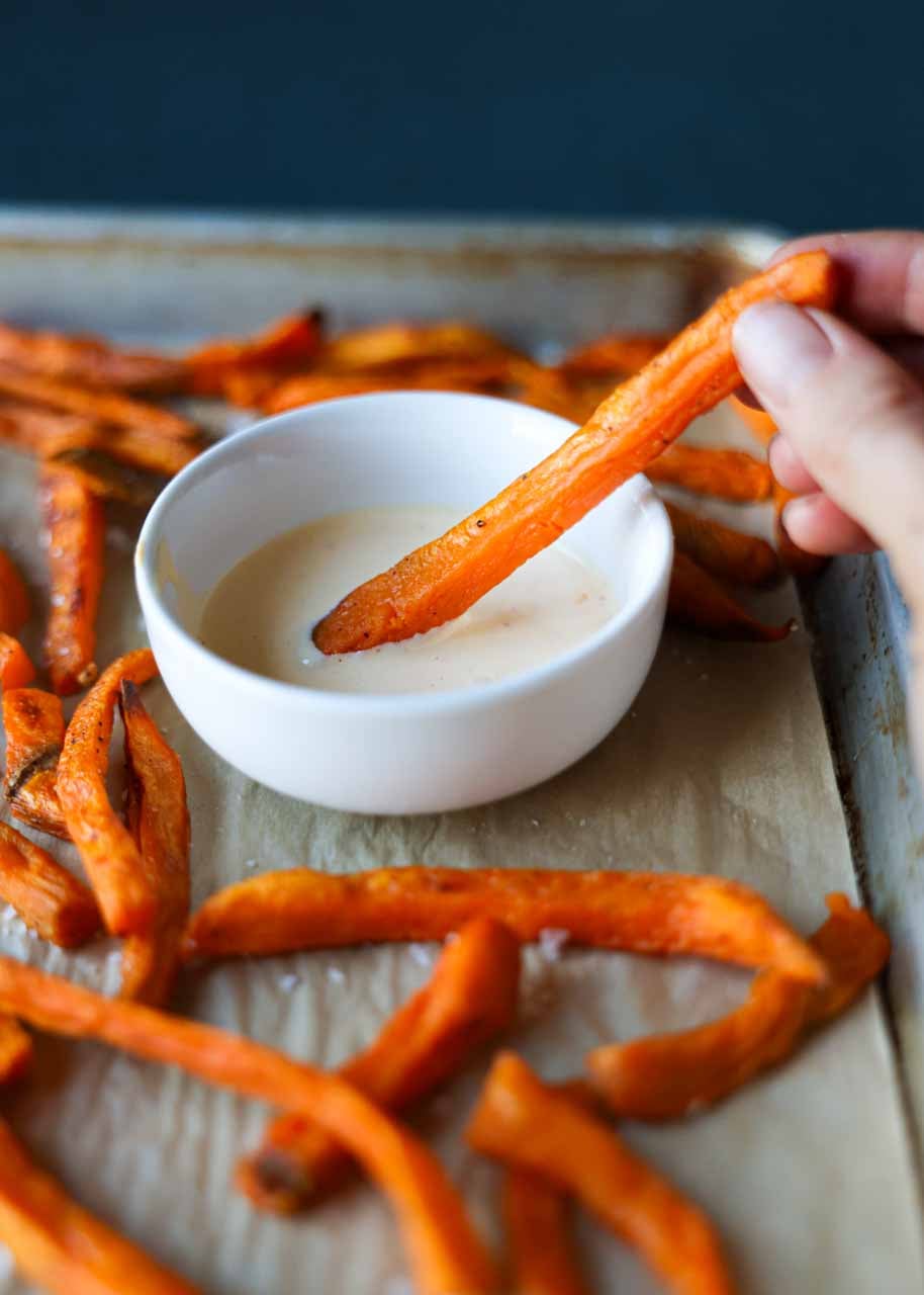 Cooked from frozen sweet potato fries are being dipped in a sauce.