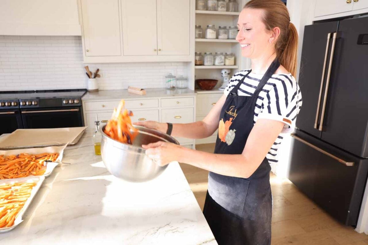 Becky tosses sweet potatoes in a mixing bowl with oil.