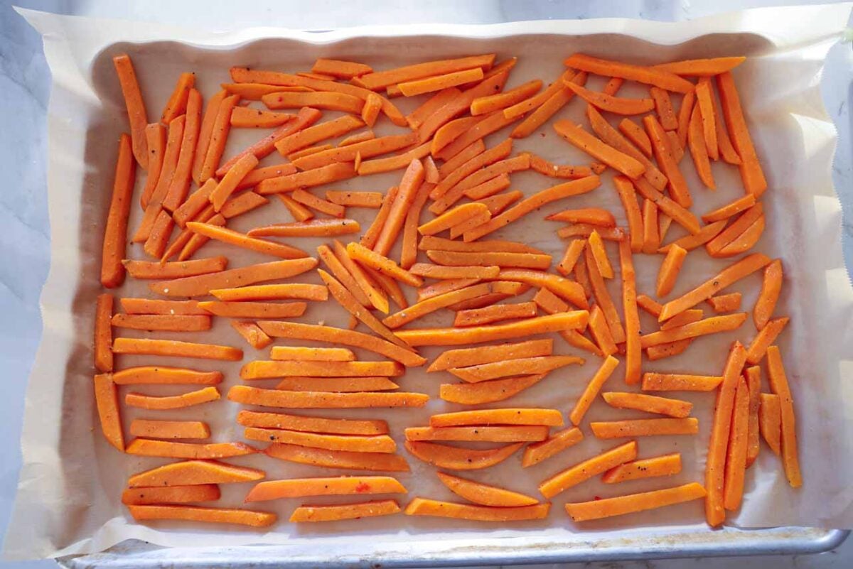 The seasoned and blached sweet potato fries are placed on a baking sheet and put in the freezer.