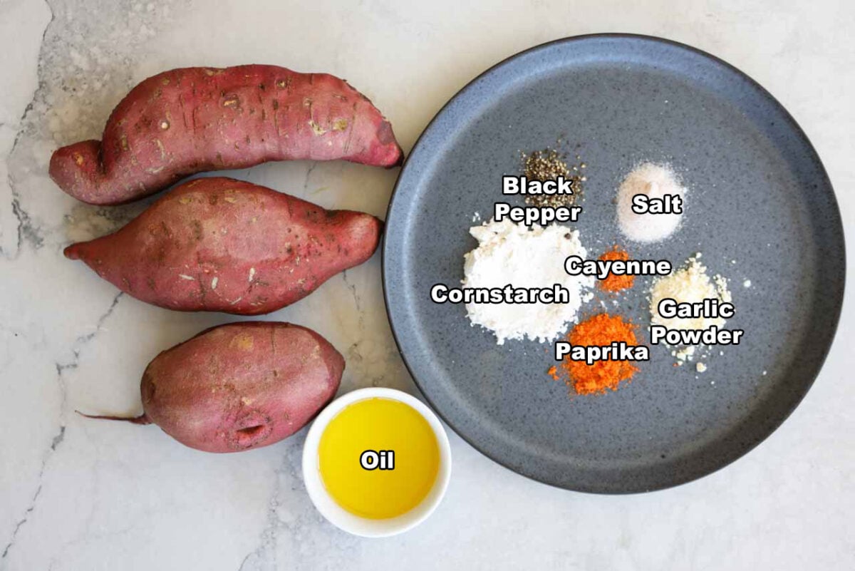 Ingredients for the sweet potato fries are laid out. There is sweet potatoes, oil, cornstarch, and various seasonings on a plate.