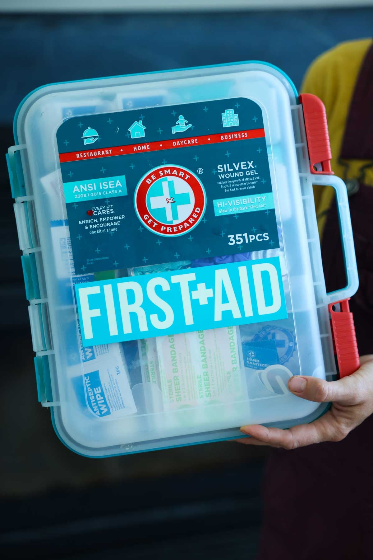 A basic first aid kit for a car or home is being held up for display.