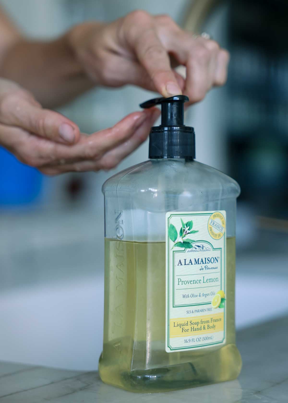 Hands press down a pump on a hand soap container.