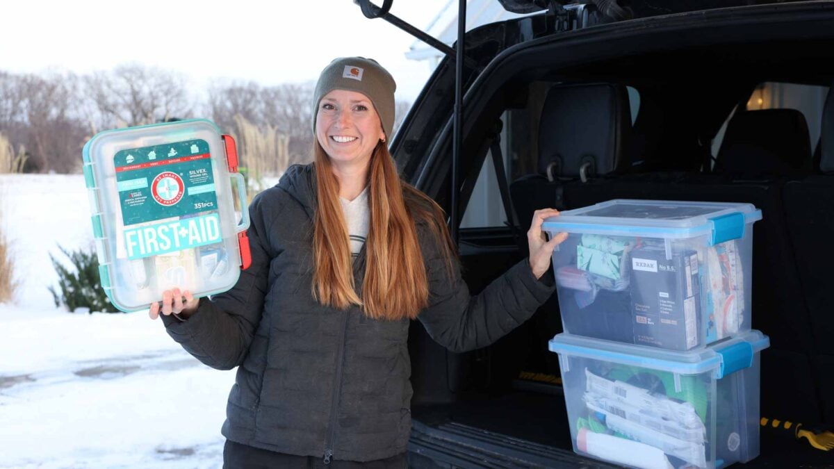 Becky outside of her car showing a first aid kit and two boxes of emergency car items.