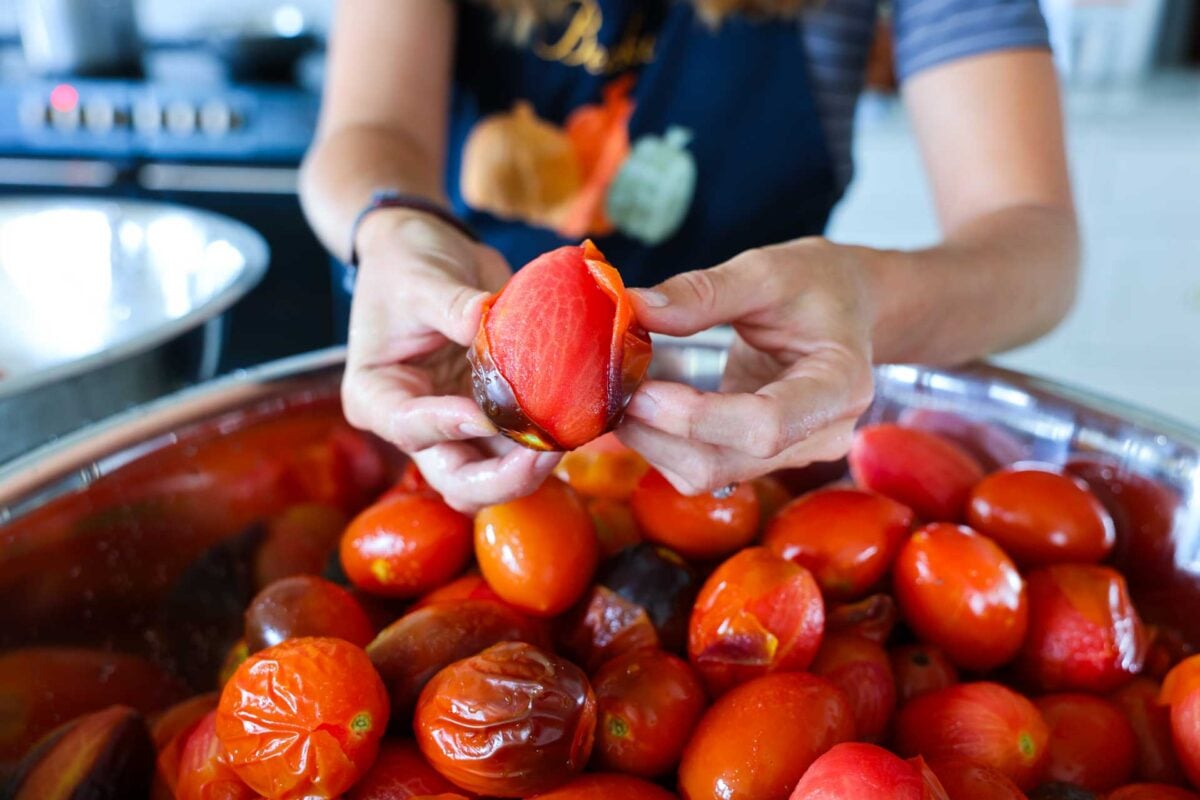 Hands hold up a tomato showing how easy it is to peel of tomato skins after a boiling water dip.